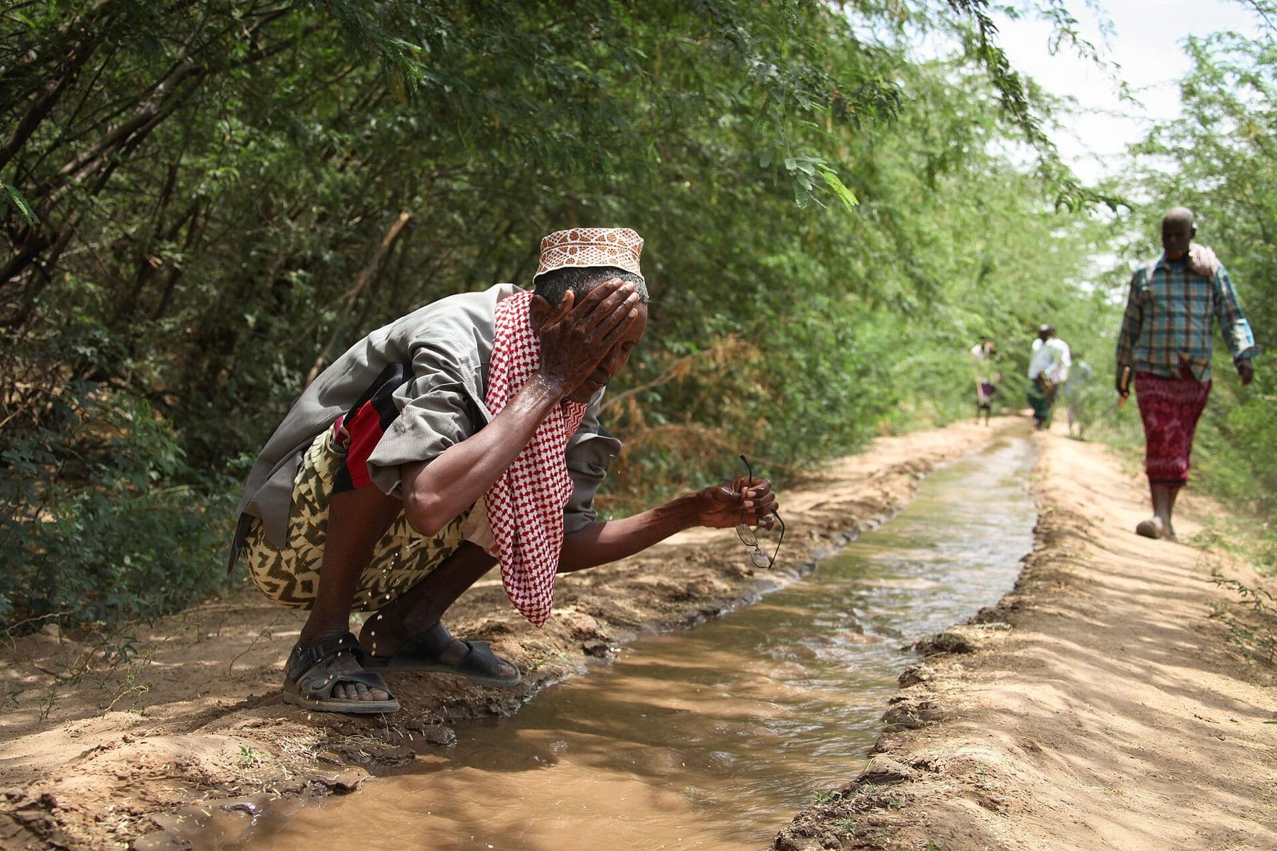 An elder washing at a tree-lined irrigation canal fed by the Shabelle
